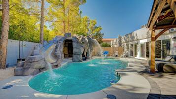A swimming pool with a waterfall feature, surrounded by trees and a covered patio area.