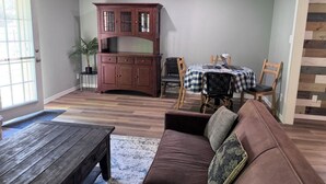 Uma sala de estar com um sofá marrom, uma mesa de centro de madeira, uma mesa de jantar com cadeiras e um armário de madeira.