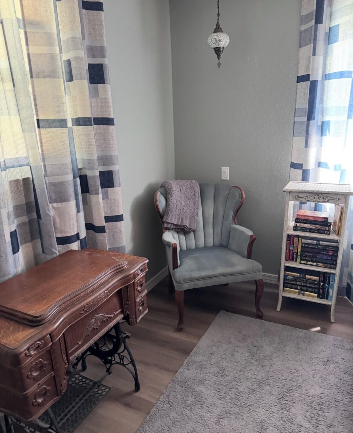 A room with a wooden desk, a cushioned armchair, a bookshelf, and a patterned rug.
