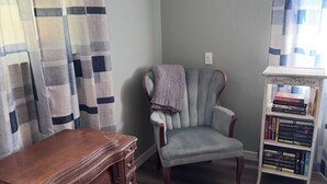 Um quarto com uma escrivaninha de madeira, uma poltrona estofada, uma estante de livros e um tapete estampado.