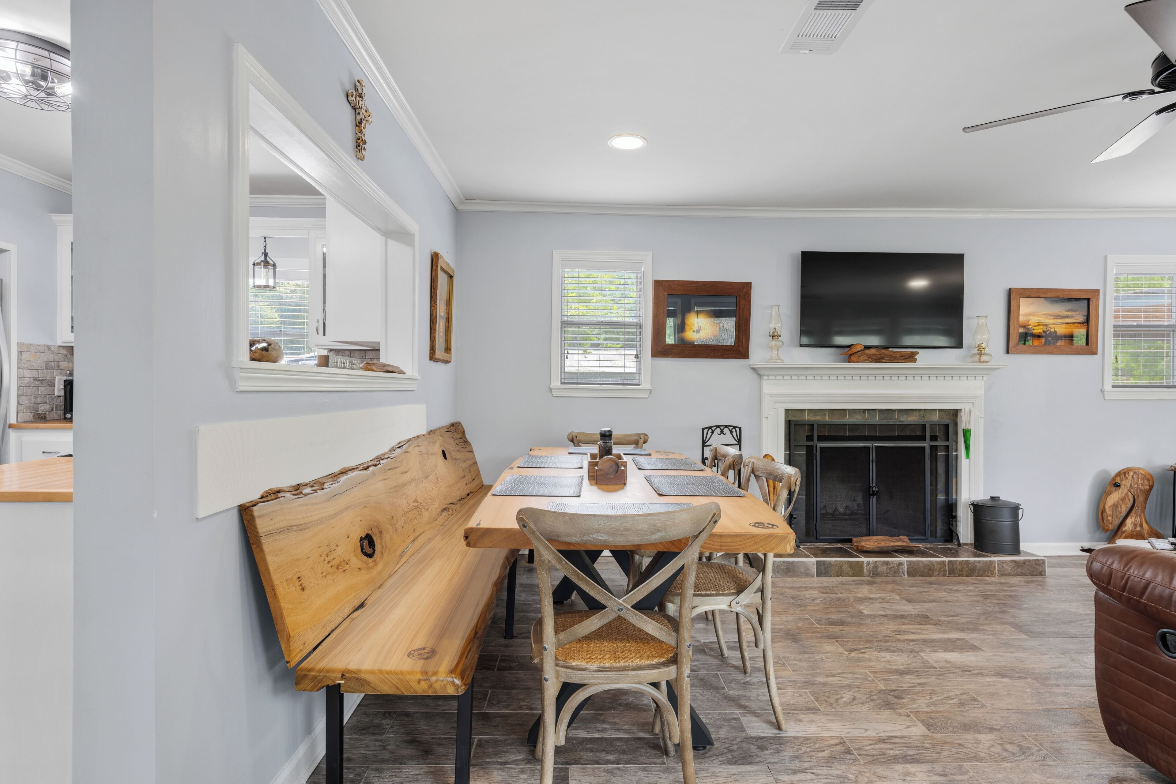 A dining area with a wooden bench, chairs, a table, a fireplace, and a television mounted above it.