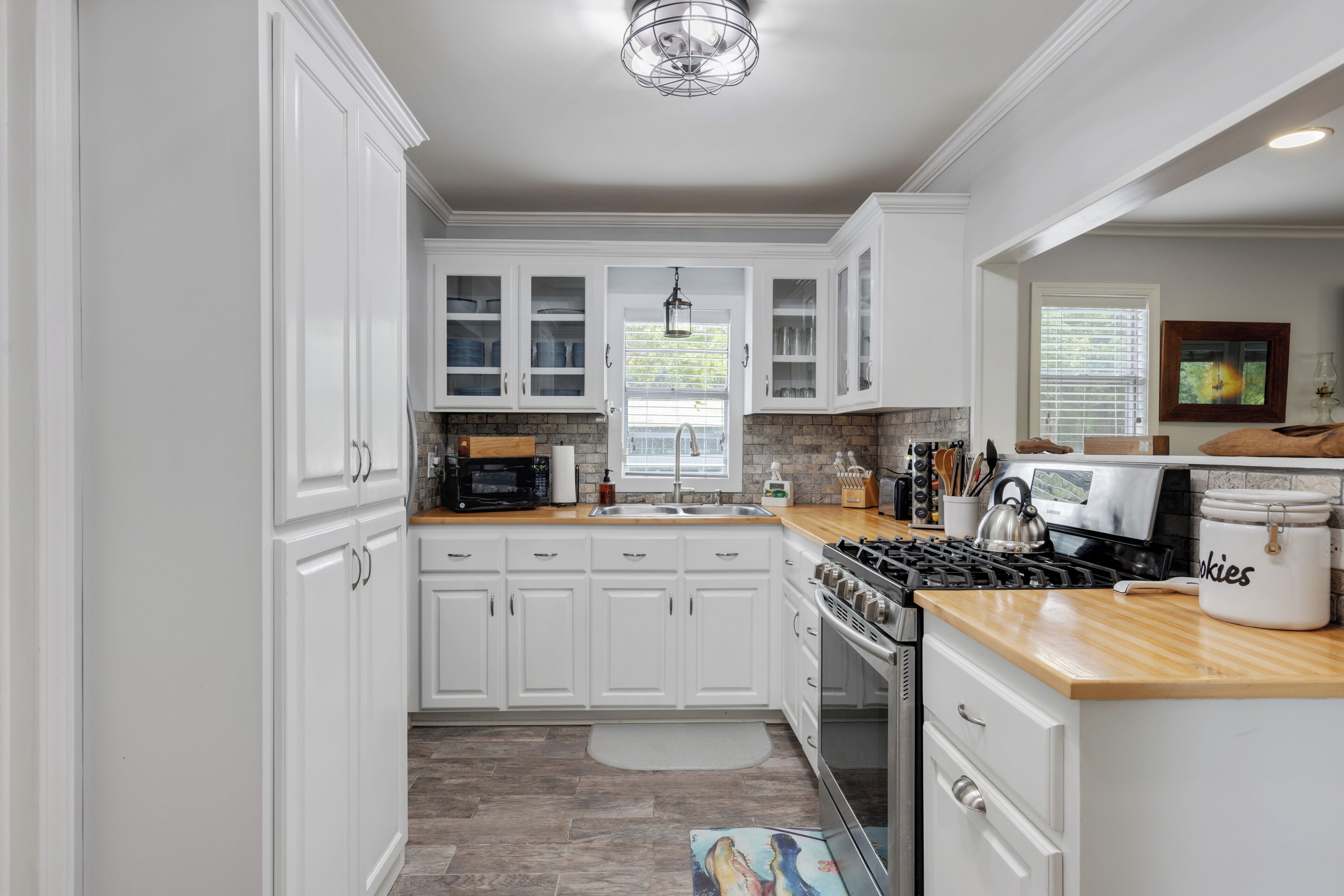 A modern kitchen with white cabinetry, a stainless steel stove, and a window with blinds.