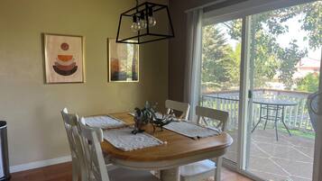 A dining area with a wooden table, white chairs, and a view of a balcony with outdoor furniture.