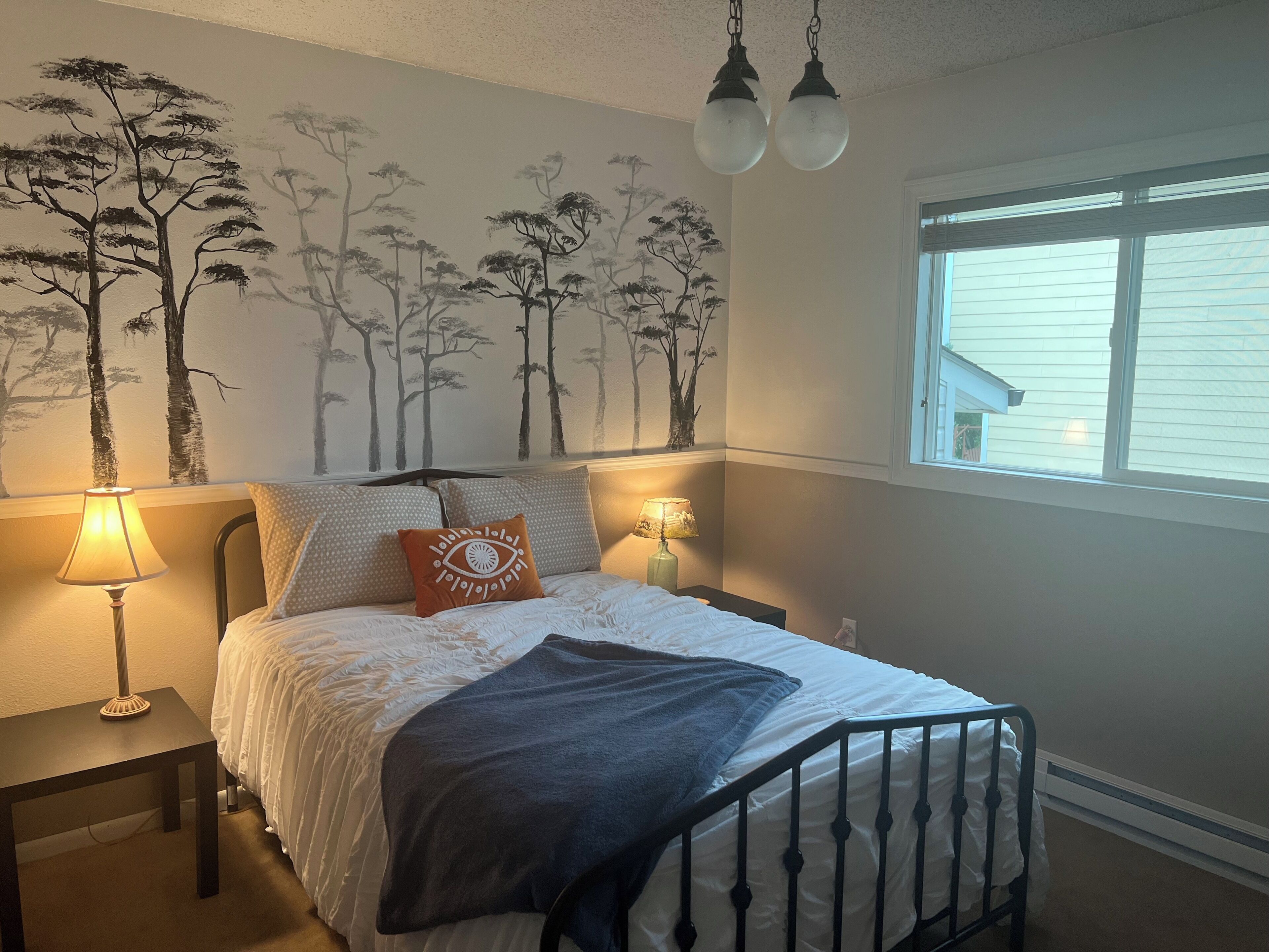 A bedroom with a bed, two bedside lamps, a window, and a wall mural.