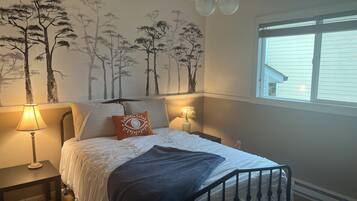 A bedroom with a bed, two bedside lamps, a window, and a wall mural.