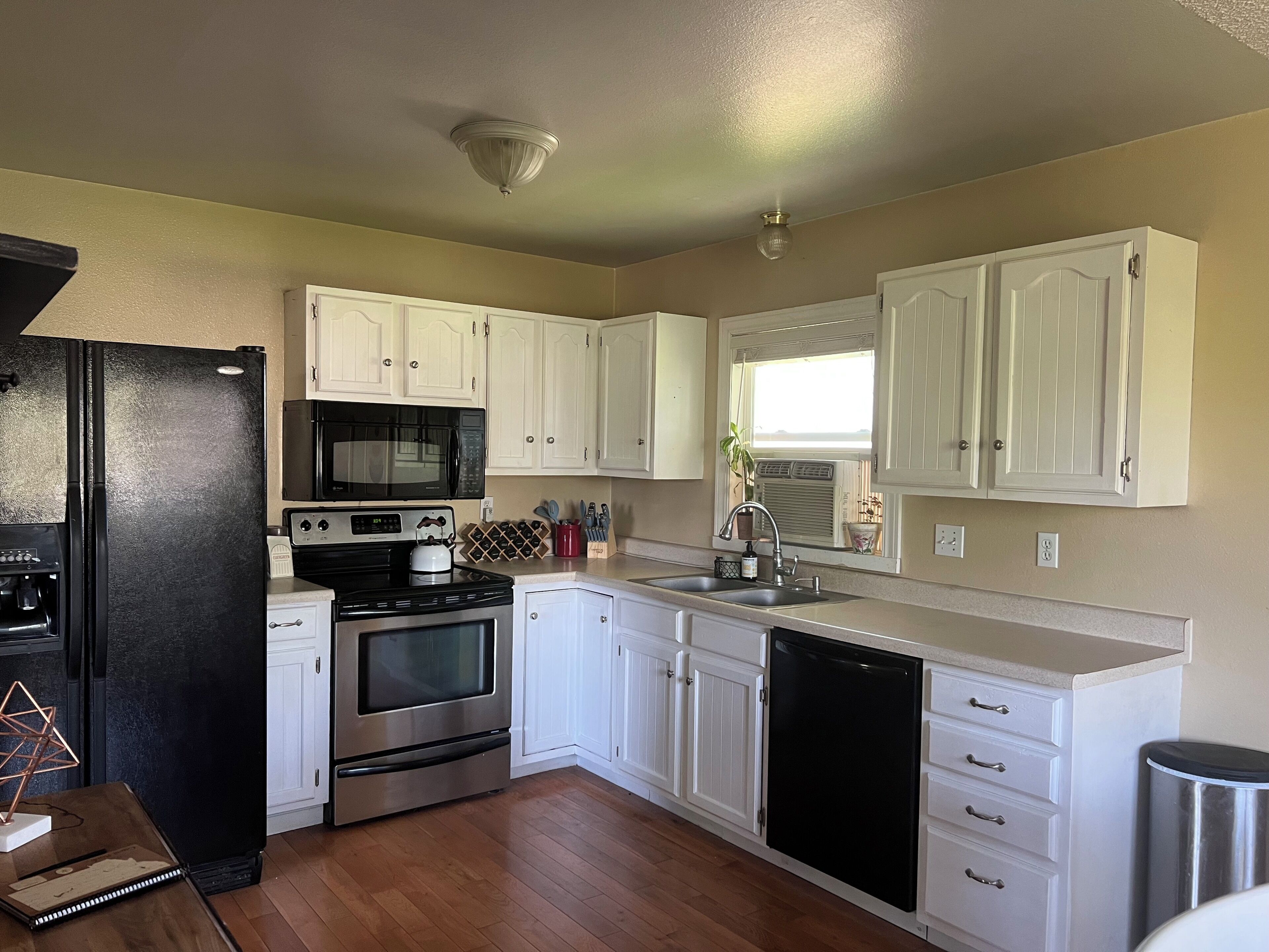 A kitchen with white cabinets, a black refrigerator, a microwave, an oven, a sink, and a dishwasher.