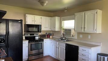 A kitchen with white cabinets, a black refrigerator, a microwave, an oven, a sink, and a dishwasher.