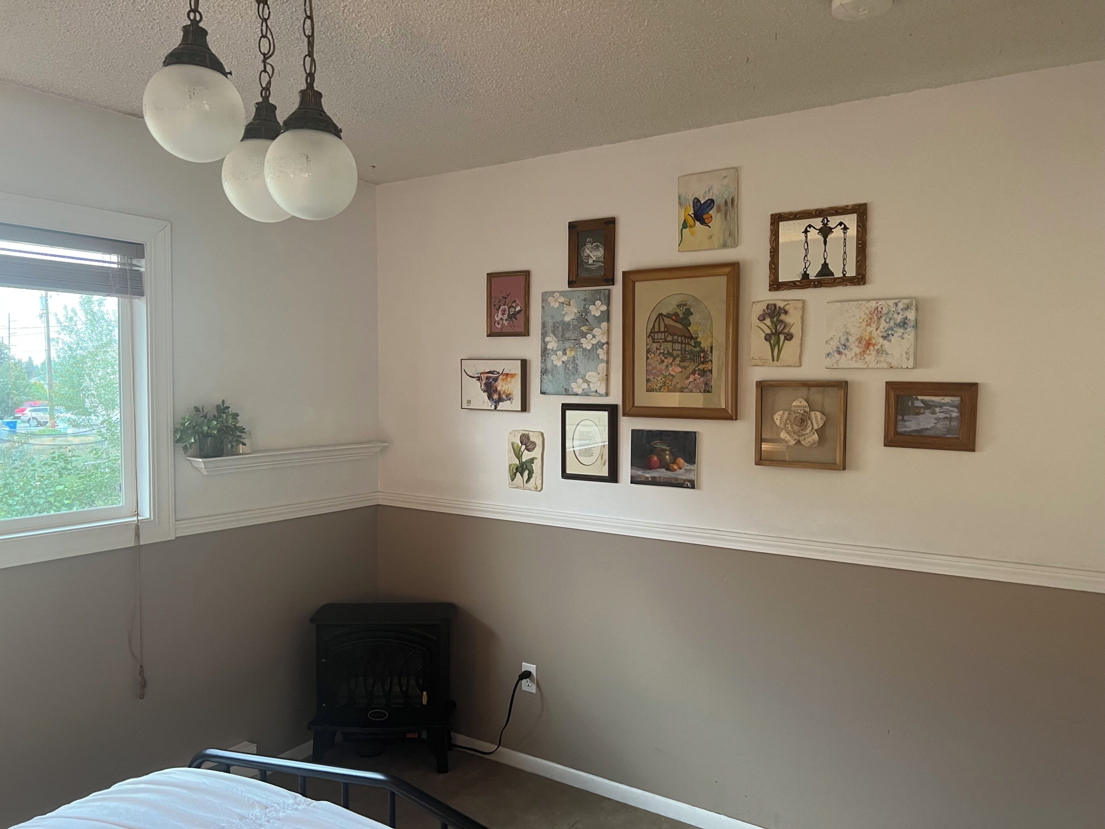 A bedroom with a bed, a wall-mounted heater, and various framed artworks.
