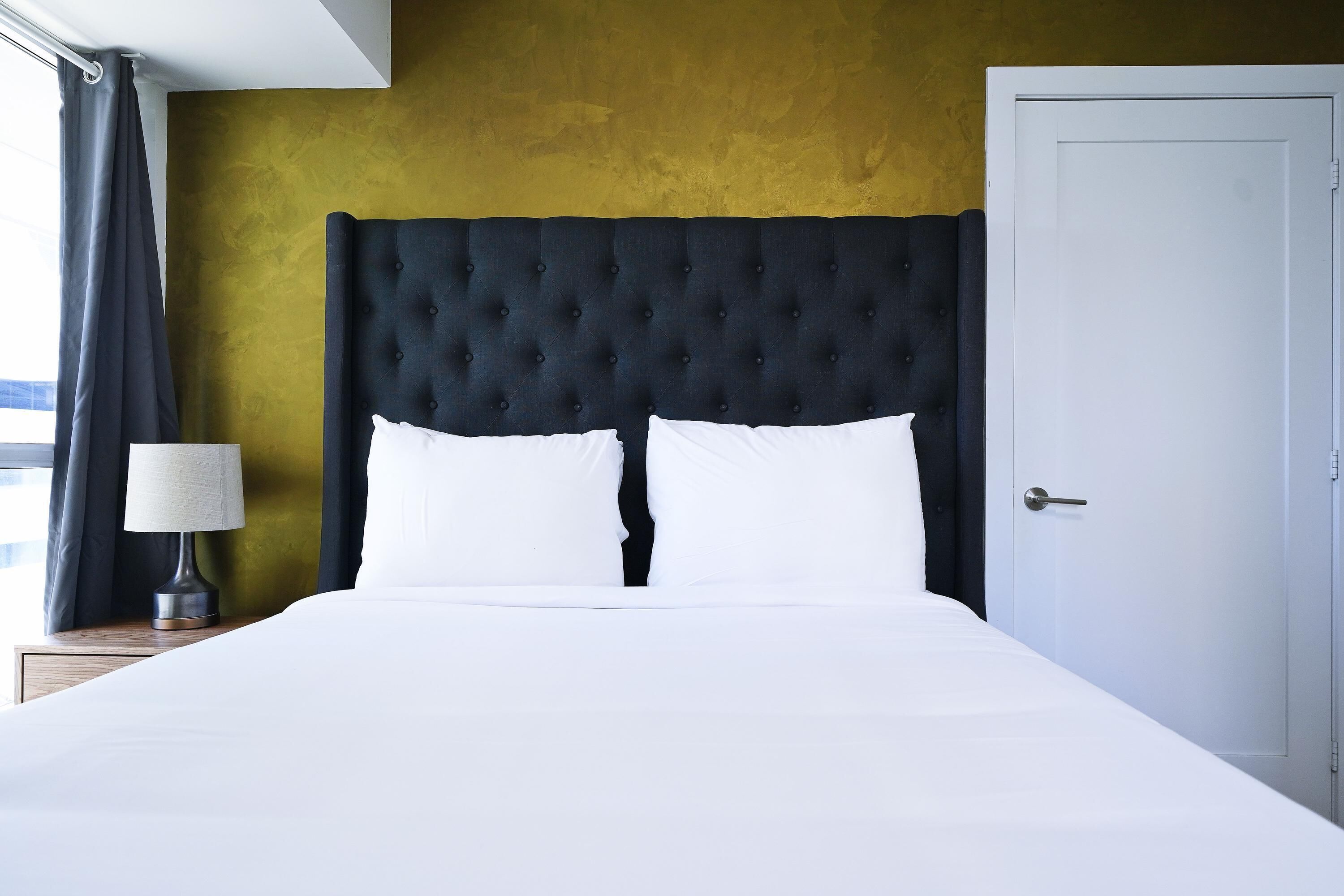 Ein Bett mit einer gepolsterten Kopfteil, einer Nachttischlampe und einer Tür auf der rechten Seite.