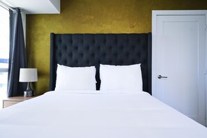 A bed with a tufted headboard, a bedside lamp, and a door to the right.