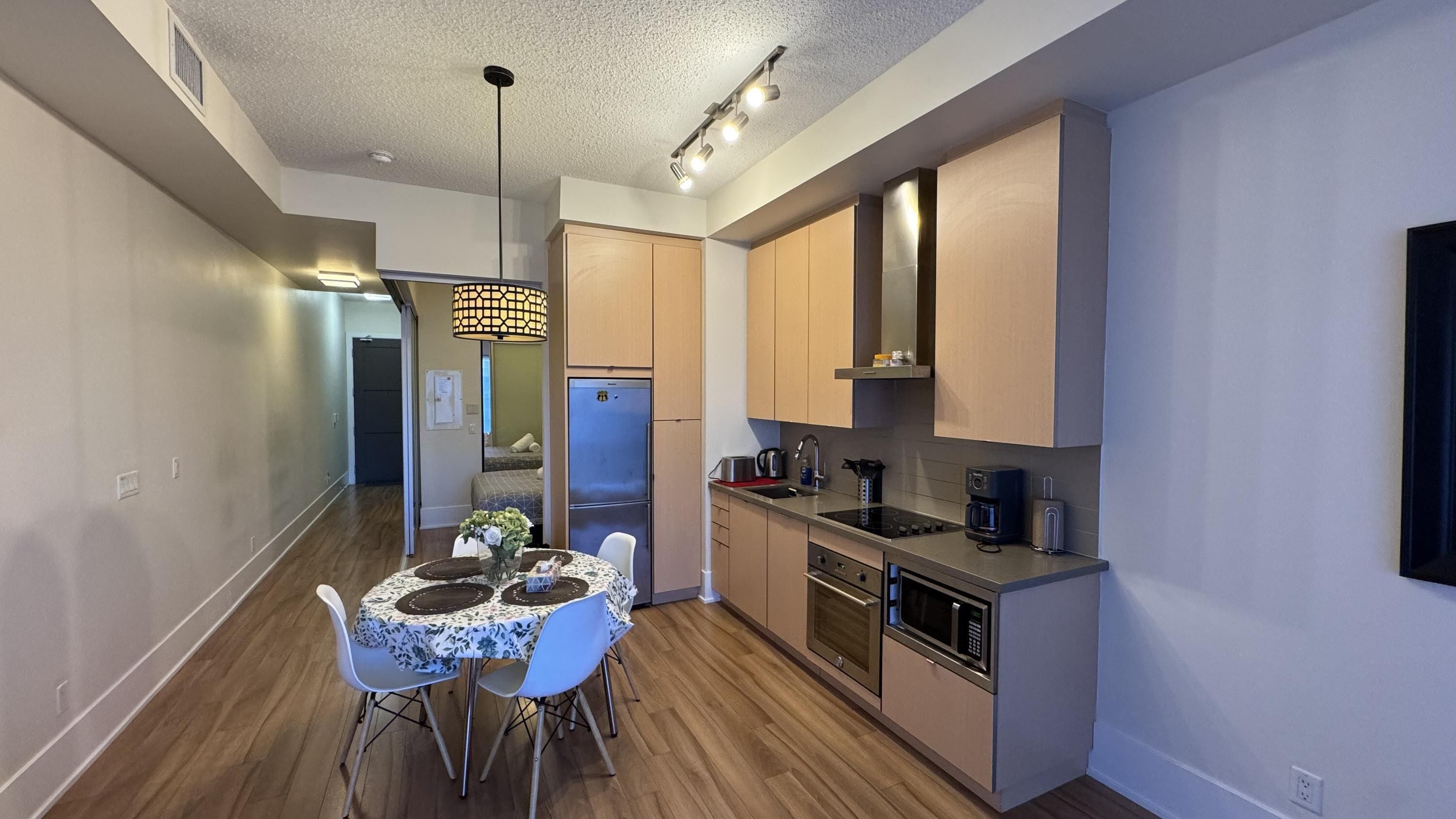 A compact kitchen with modern appliances, a dining area with a table and chairs, and a visible bed in the adjacent room.