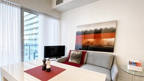 Habitación de hotel moderna con zona de comedor, sofá, televisión y un cuadro en la pared.