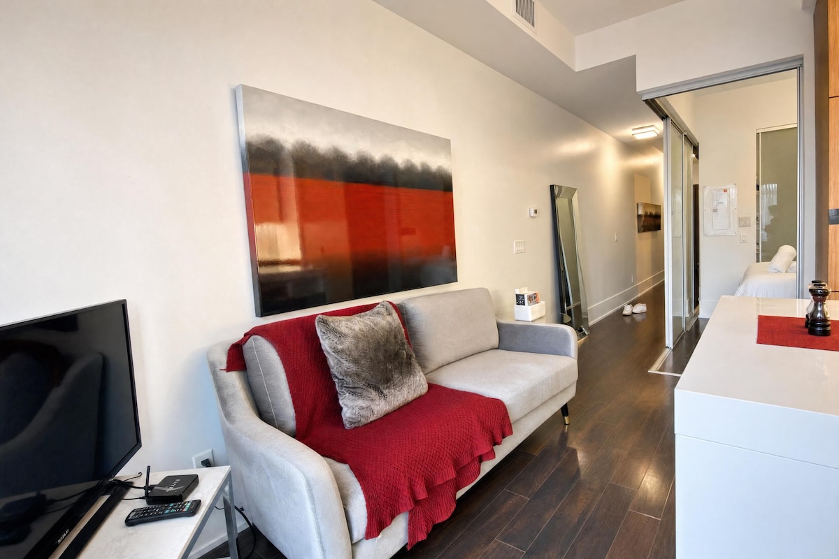 A modern living room with a sofa, a flat-screen TV, a coffee table, and a large abstract painting on the wall.