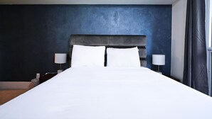 Una habitación de hotel con una cama grande, dos lámparas de noche y una pared azul oscuro.