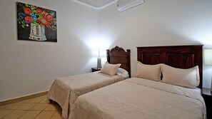 Une chambre avec deux lits, une table de chevet, une lampe et un tableau au mur.