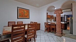 Un espace repas comprenant une table et des chaises, un tableau encadré au mur et une colonne au centre.