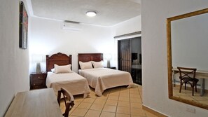 Ein Hotelzimmer mit zwei Betten, einem Schreibtisch, einem Stuhl, einem Spiegel und einer Schiebetür.