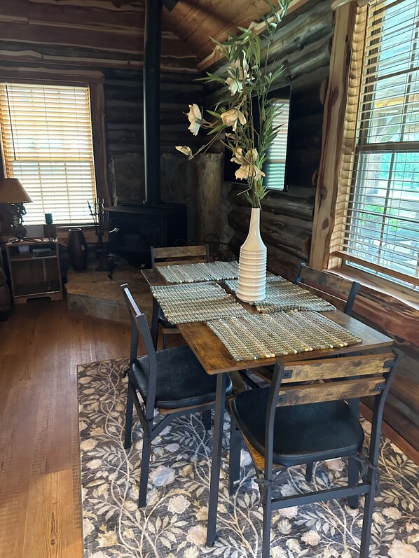 A rustic wooden interior with a dining table set for four, surrounded by chairs, and a vase with flowers on the table. - cozy mountain retreat with wood stove and hot tub (Mena)