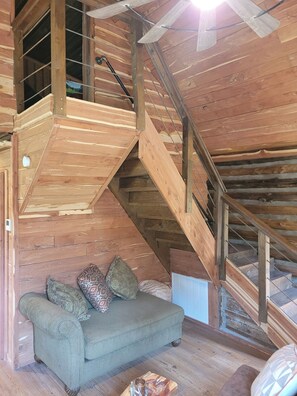 A wooden interior with a staircase, a sofa with cushions, and a radiator.