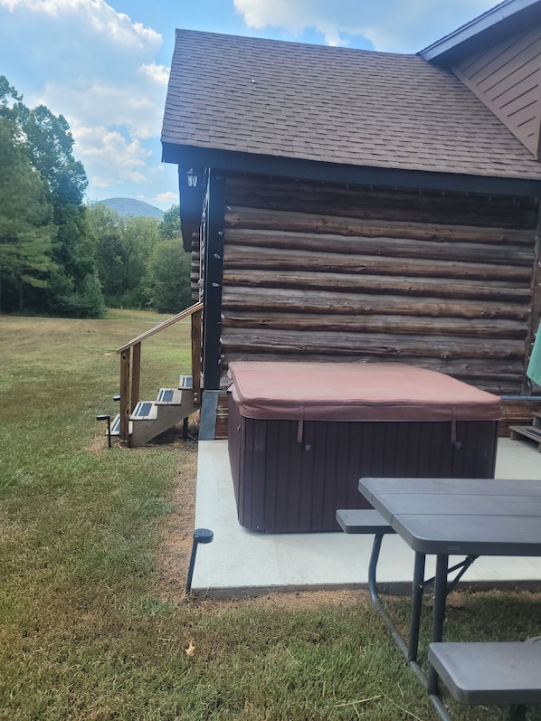 A wooden cabin with a covered patio area, including a hot tub and picnic tables.