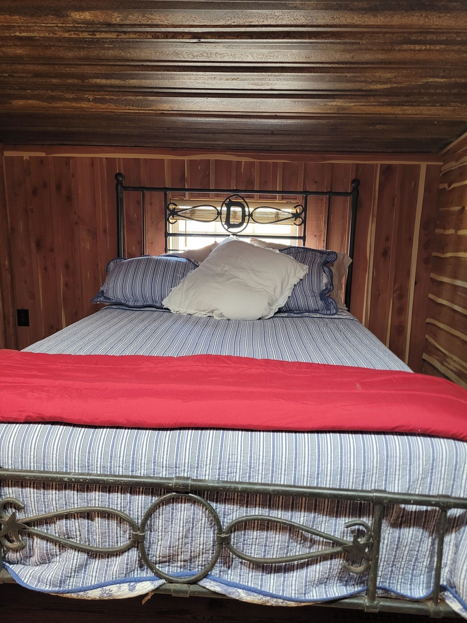 Una cama con cabecera de metal, ropa de cama a rayas y una manta roja.