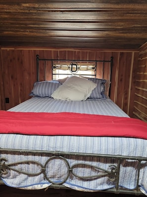 A bed with a metal headboard, striped bedding, and a red blanket.