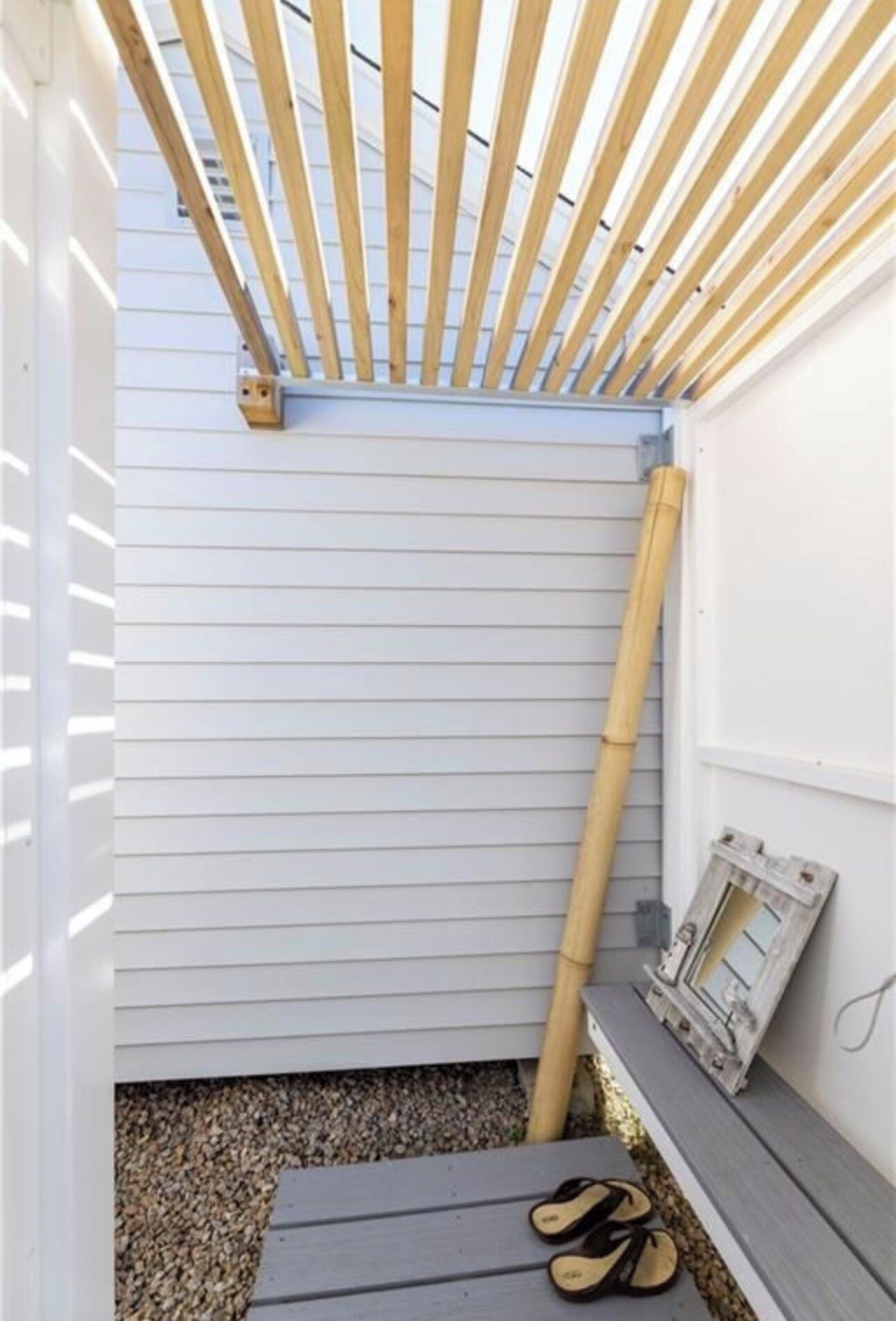 A corner of a room with a wooden ceiling structure, a window with a shutter, and a pair of sandals on the floor.