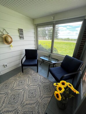 A room with a large window, two chairs, a small table, a rug, and a vase with sunflowers. - Vintage Charm Near Pilot Mountain and Mount Airy (Westfield)