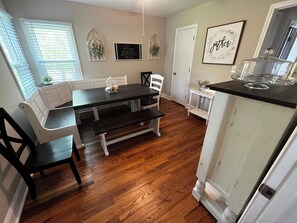 Un coin repas avec une table en bois foncé, des bancs blancs et un buffet blanc surmonté d’un plateau en verre.