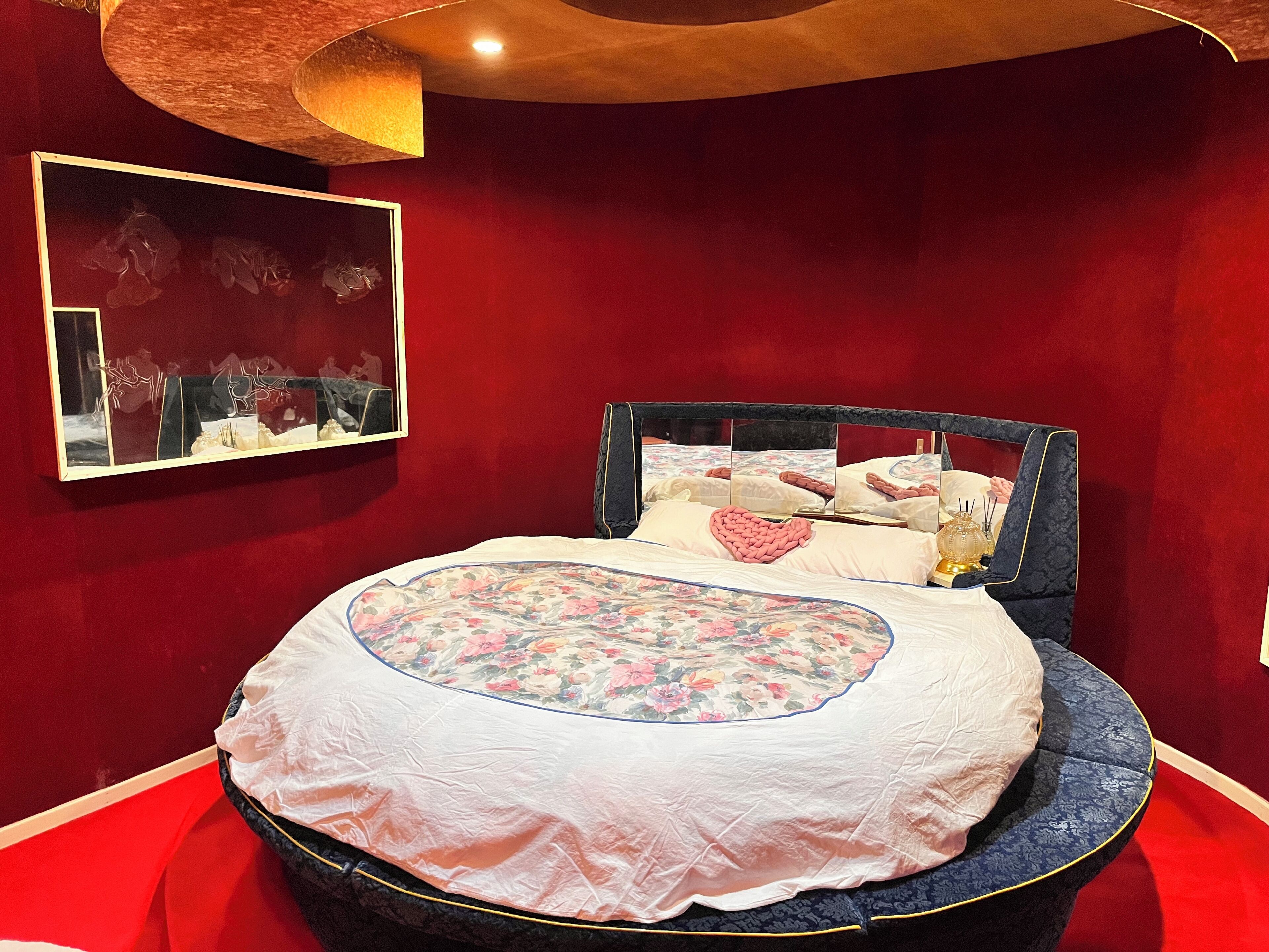 A bed with a floral bedspread, a mirror, and a red wall.