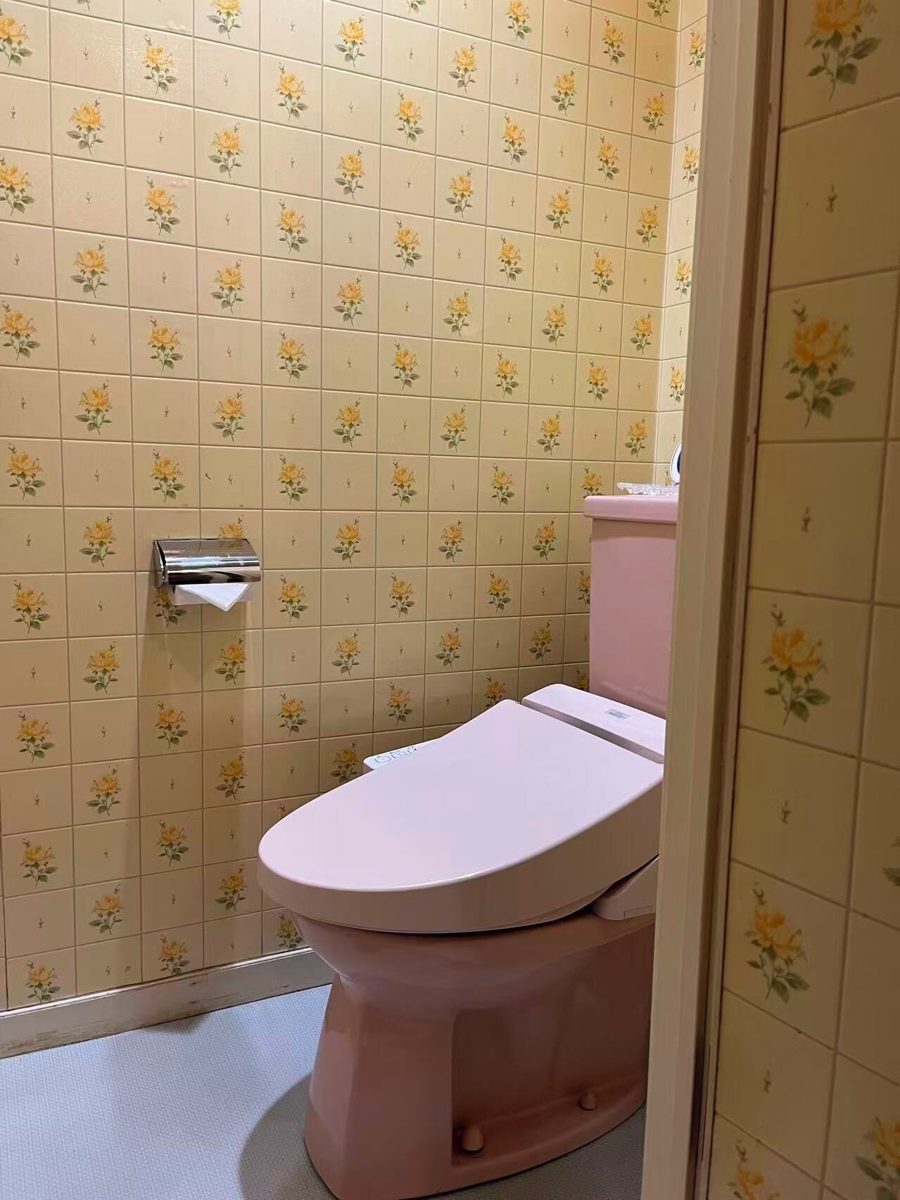 Un baño con inodoro, secamanos y pared con un estampado de flores.