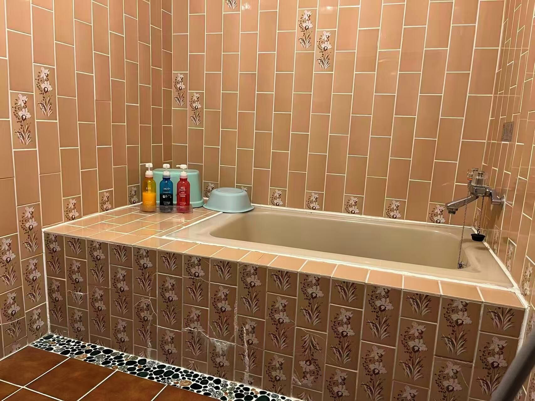 A bathroom with a bathtub, floral patterned tiles, and a set of toiletries on the counter.