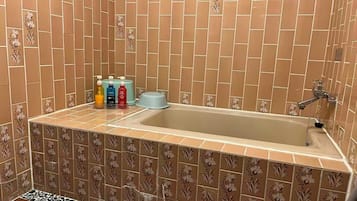 A bathroom with a bathtub, floral patterned tiles, and a set of toiletries on the counter.