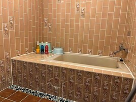 A bathroom with a bathtub, floral patterned tiles, and a set of toiletries on the counter.
