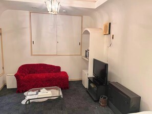 A room with a red sofa, a television, a white wardrobe, and a small table with a tissue box.