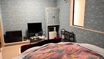 A bedroom with a bed, a television, a microwave, a small refrigerator, a mirror, and a window.