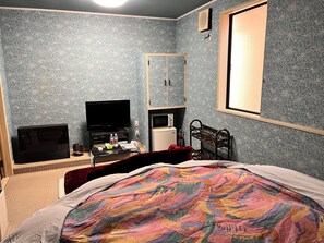 Een slaapkamer met een bed, een televisie, een magnetron, een kleine koelkast, een spiegel en een raam.