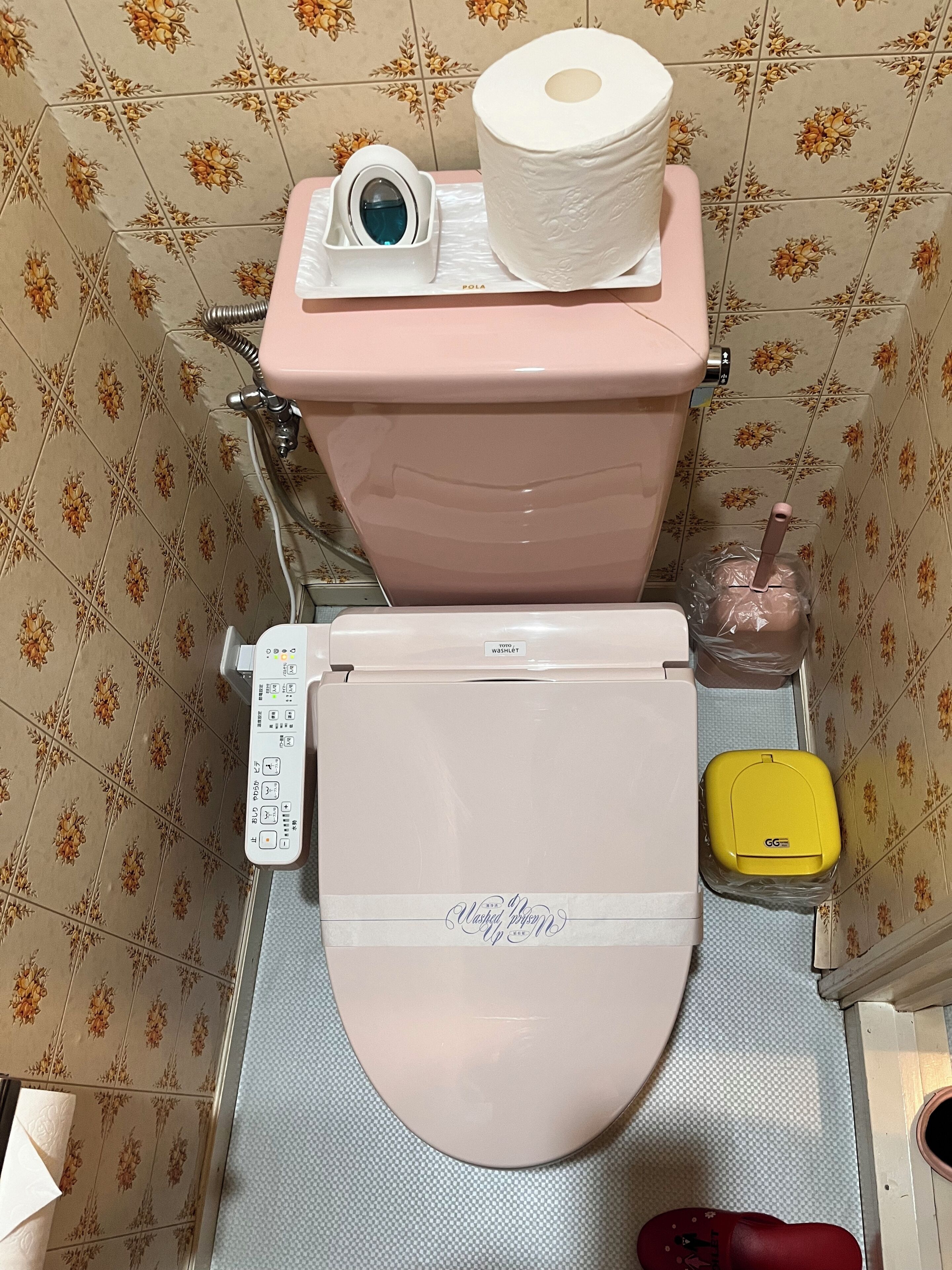 A toilet with a control panel, a toilet paper holder, and a yellow waste bin.