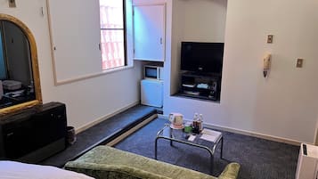 A hotel room with a bed, a television, a small kitchenette, and a seating area with a table and chairs.
