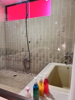 Baño con bañera, ducha y paredes de azulejos.