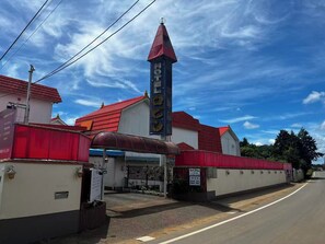 A hotel with a prominent red roof, a tall blue sign with the hotel's name, and a small bell on top.