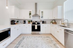 A modern kitchen with white cabinetry, a stainless steel range, and a patterned rug. - Townhaus 205 | River Ranch 2 Master Suites (Lafayette)