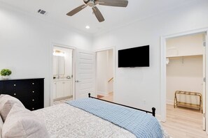 A bedroom with a bed, a dresser, a ceiling fan, a TV, and a walk-in closet. - Townhaus 205 | River Ranch 2 Master Suites (Lafayette)