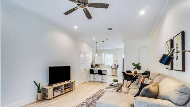 A modern living room with a flat-screen TV, a sofa, and a dining area with a table and chairs. - 3 BD Designer Townhaus | River Ranch & Shopping (Lafayette)