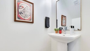A bathroom with a white sink, a mirror, a framed picture on the wall, and a small potted plant. - 3 BD Designer Townhaus | River Ranch & Shopping (Lafayette)
