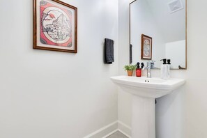 Ein Badezimmer mit Waschbecken, Spiegel, einem gerahmten Bild an der Wand und einem kleinen Topfpflanzen.