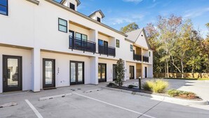 A multi-story residential building with balconies, a parking area, and a landscaped garden. - 3 BD Designer Townhaus | River Ranch & Shopping (Lafayette)
