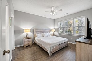 A bedroom with a bed, bedside lamps, a ceiling fan, a window with blinds, and a TV on a wooden cabinet. - Ocean Keyes 3BR First Floor Condo - North Myrtle Beach (North Myrtle Beach)