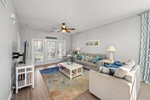 A living room with a white sofa, a coffee table, a TV, and a ceiling fan. - Ocean Keyes 3BR First Floor Condo - North Myrtle Beach (North Myrtle Beach)