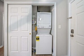 Une buanderie équipée d’un lave-linge et d’un sèche-linge, avec une porte et une étagère contenant des produits de nettoyage.